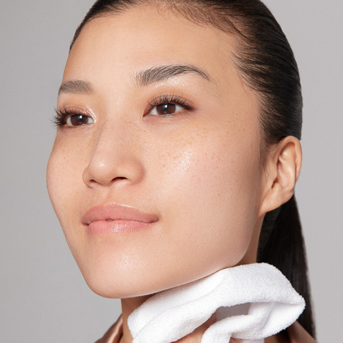 Headshot of a model dabbing her cleansed face with a white towel